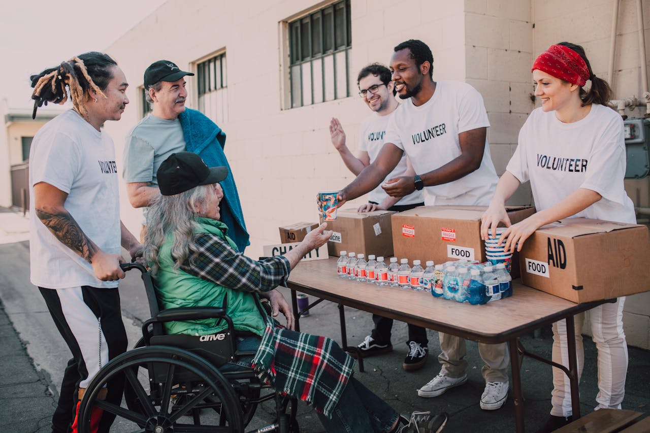 about-us-01 Volunteers distribute bottled water and supplies to diverse individuals in an outdoor setting, showcasing community support.